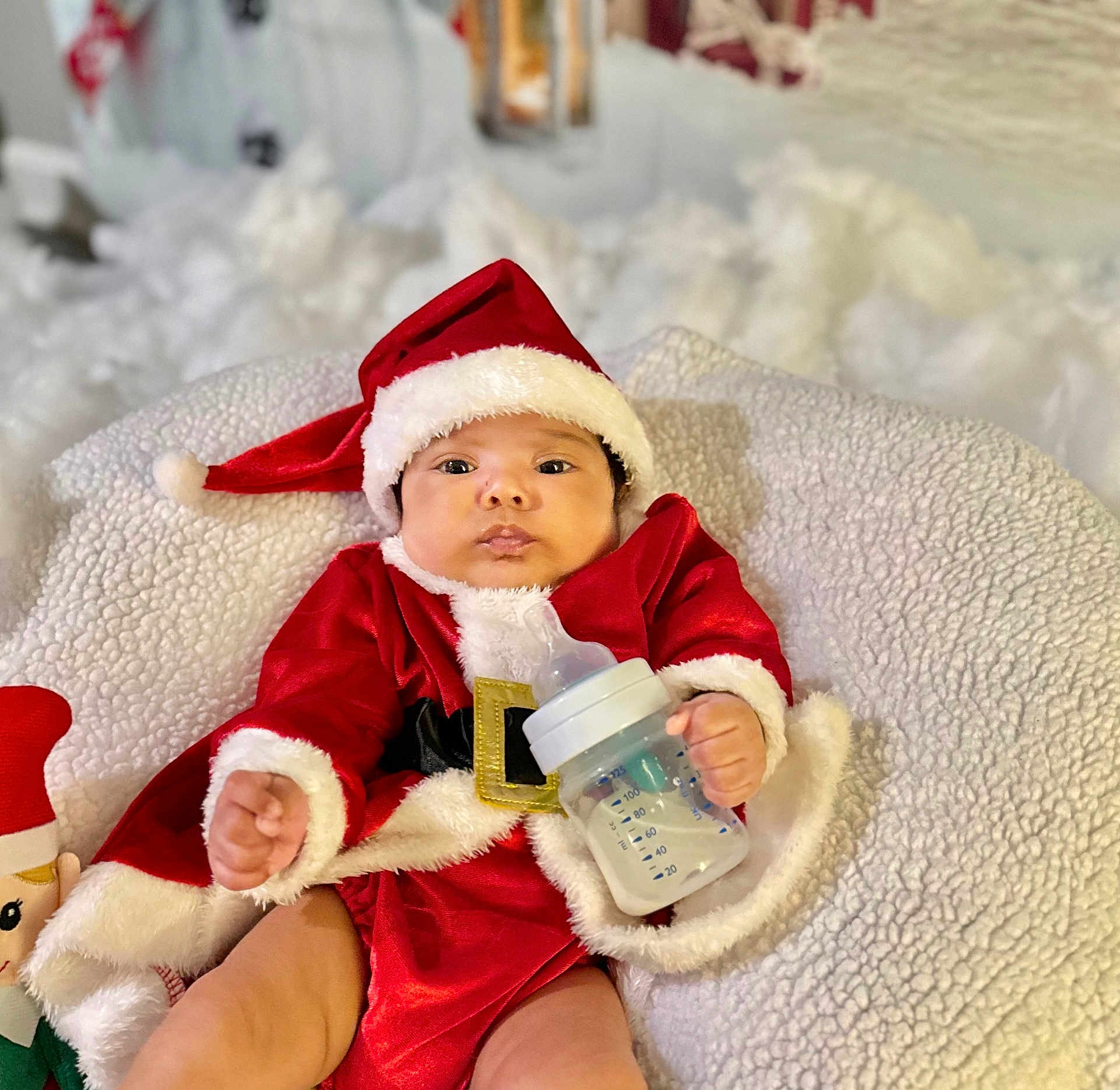 Amanda is registered to the contest to win money with this photo: baby, infant, christmas, santa_claus, holiday, bottle, milk, red_clothing, hat, blanket, plush, toy, cute, face, person, indoors, festive, child, smile, christmas_costume