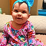 Gemma is registered to the contest to win money with this photo: baby, child, smiling, headband, blue_bow, colorful_clothing, cartoon_print, sitting, indoors, bed, cozy, happy, portrait, cute, infant, person, face, apparel, playful, young_child
