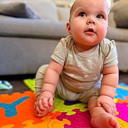 Gemma is registered to the contest to win money with this photo: baby, child, infant, cute, sitting, colorful_mat, puzzle_mat, onesie, chubby_cheeks, curious_look, indoor, living_room, couch, soft_lighting, floor, portrait, young_child, playtime, hands, feet