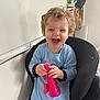 Lyzio participe au concours pour gagner de l'argent avec cette photo : baby, blue_onesie, chair, child, curly_hair, cute, fun, hands, happy, indoor, joyful, laughing, person, pink_toy, playful, portrait, seated, smiling, toddler, toy