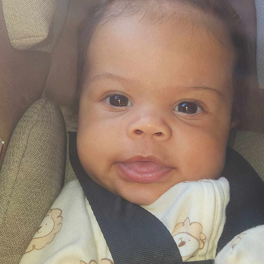 Naomi is registered to the contest to win money with this photo: baby, blanket, car, car_interior, carseat, clothing, cushion, dress, face, furniture, happy, head, homedecor, newborn, person, photography, portrait, smile, transportation, vehicle
