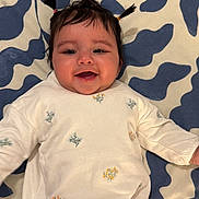 Ayla is registered to the contest to win money with this photo: baby, child, infant, smiling, happy, portrait, lying_down, pigtails, hair, face, eyes, mouth, clothing, shirt, pants, floral_pattern, blanket, indoor, close_up, family_photo