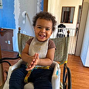Zion joined the competition — help win amazing prizes! child, toddler, high_chair, bib, smile, clapping_hands, curly_hair, face, eyes, teeth, clothing, seatbelt, food_crumbs, indoor, wooden_floor, doorway, home_interior, furniture, happy, portrait