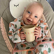 Emmie participe au concours pour gagner de l'argent avec cette photo : baby, child, smiling, bib, cup, flamingo_pattern, cushion, chair, indoor, pillow, cute, happy, person, infant, clothing, face, hand, head, blue_eyes, blanket