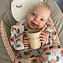 baby, child, smiling, bib, cup, flamingo_pattern, cushion, chair, indoor, pillow, cute, happy, person, infant, clothing, face, hand, head, blue_eyes, blanket