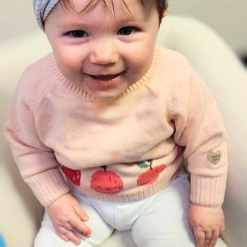 Raelynn joined the competition — help win amazing prizes! baby, baby_girl, bow, child, clothing, cute, face, furniture, happy, headband, indoor, infant, person, portrait, sitting, smile, soft_texture, sweater, white_pants, young_child