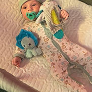 Brandon is registered to the contest to win money with this photo: baby, infant, pacifier, plush_toy, onesie, hat, bed, mattress, sleeping_area, child, cute, soft_toys, animal_print, indoor, comfort, lying_down, pastel_colors, warm_lighting, face, hand