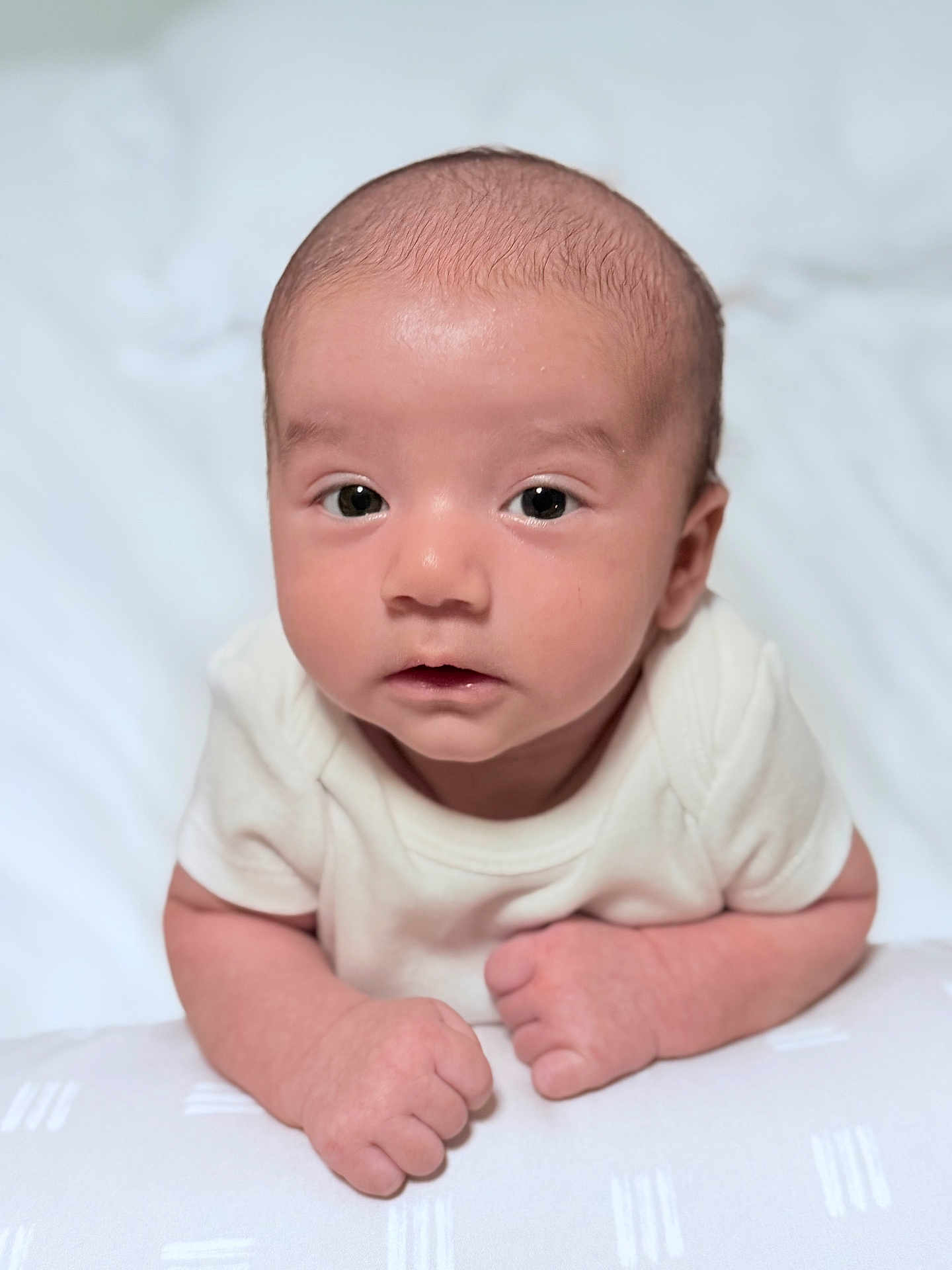 Keyhan joined the competition — help win amazing prizes! baby, infant, tummy, hands, fists, white_clothing, soft_skin, face, eyes, curious, lying_down, indoors, blanket, head, portrait, newborn, cute, child, person, closeup