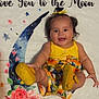 baby, child, smiling, yellow_clothing, floral_pattern, blanket, crescent_moon, flowers, happy, cute, infant, portrait, indoors, playful, colorful, footwear, headband, person, skin, face