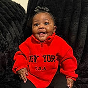 Kemora joined the competition — help win amazing prizes! baby, child, smiling, red_fleece, black_bow, sitting, couch, indoor, happy, portrait, person, furniture, black_pants, cute, young_child, warm_clothing, cozy, bright_color, expression, infant