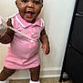 baby, child, pink_dress, white_shoes, smiling, indoor, carpet, wall, standing, happy, face, person, cute, young_child, holding_object, footwear, fashion, portrait, toddler, playful