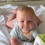 Max is registered to the contest to win money with this photo: baby, infant, child, smile, face, necklace, light_clothing, blanket, bedroom, indoors, cute, chubby_cheeks, curious, lying_down, soft_light, white_blanket, head, arms, feet, cozy