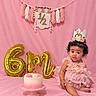 baby, child, birthday, birthday_cake, pink, gold, balloons, number_six, crown, floral, dress, curly_hair, sitting, smiling, portrait, studio, backdrop, party, decoration, cake_stand