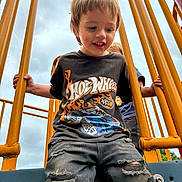 Uhtred is registered to the contest to win money with this photo: child, boy, playground, yellow_bars, hot_wheels_tshirt, ripped_jeans, outdoor, cloudy_sky, smiling, playing, person, hands, metal_structure, casual_clothing, happy, daylight, park, friends, fun, jeans