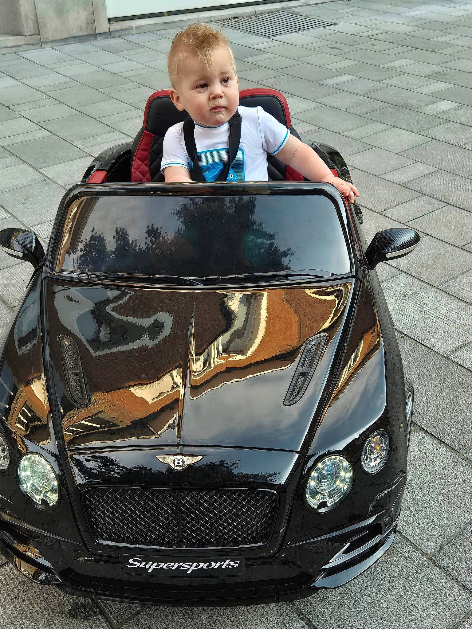 Tiyo participe au concours pour gagner de l'argent avec cette photo : automotive_design, automotive_exterior, automotive_fog_light, automotive_lighting, automotive_mirror, automotive_parking_light, automotive_tire, bumper, car, green, grille, headlamp, hood, motor_vehicle, person, personal_luxury_car, photograph, rim, tints_and_shades, toddler