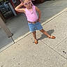 braids, brown_shoes, building, casual, child, concrete, confident, denim_shorts, fashion, girl, glass_doors, necklaces, outdoor, pink_sunglasses, pink_top, posing, posters, ribbons, sidewalk, summer