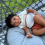 Krishiv is registered to the contest to win money with this photo: toddler, child, smiling, swing, cushion, outdoor, grass, pebbles, happy, curly_hair, white_shirt, orange_shorts, relaxing, playful, portrait, baby, seat, daylight, person, casual