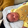 Eden a rejoint le concours — aidez-le/la à gagner de superbes lots ! baby, sleeping, infant, yellow_onesie, dinosaur_pattern, blanket, cushion, soft_texture, indoors, resting, peaceful, cozy, child, newborn, portrait, face, head, clothing, comfort, relaxation