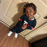 Vamir is registered to the contest to win money with this photo: child, smiling, standing, indoor, door, wooden_floor, casual_clothing, sneakers, hairstyle, person, young, happy, fashion, portrait, playful, confident, home, shadow, floor, wall