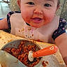 baby, child, high_chair, bib, food, messy, smiling, face, spoon, bowl, meal, indoor, cute, happy, feeding, clothing, table, expression, toddler, eating