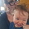 Zoë joined the competition — help win amazing prizes! adult, blue_clothing, buttoned_sweater, casual, child, curly_hair, earrings, face, family, glasses, happy, indoor, person, playing, portrait, smile, toddler, warm_light, window, wooden_wall