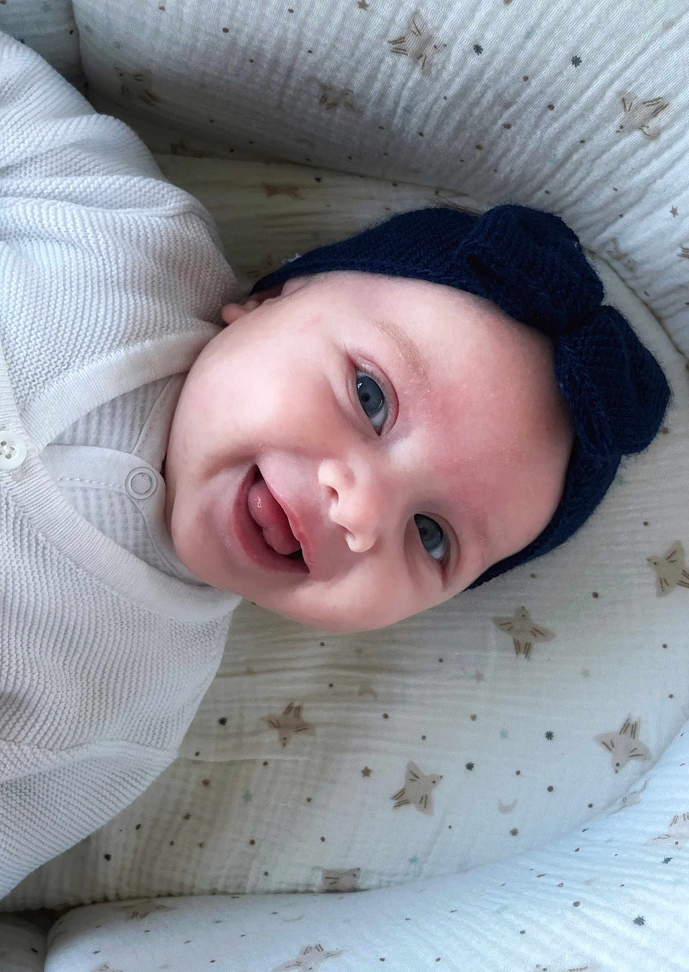 Aria participe au concours pour gagner de l'argent avec cette photo : baby, infant, smiling, headband, blue_eyes, blanket, swaddle, white_clothing, portrait, closeup, crib, fabric, star_pattern, button, mouth_open, tongue, happy, cute, newborn, face