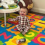 baby, plaid_pajamas, alphabet_mat, foam_mat, baby_bottle, mickey_mouse, toy, table, clothes, storage_bin, football_shaped, floor, wood_floor, corner, room, happy, smiling, sitting, child, indoor