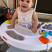 Isabella is registered to the contest to win money with this photo: baby, child, smile, walker, toy, indoor, happy, clothing, face, person, cute, infant, play, seat, footwear, hair_accessory, colorful, plastic, furniture, home
