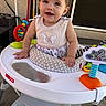 baby, child, smile, walker, toy, indoor, happy, clothing, face, person, cute, infant, play, seat, footwear, hair_accessory, colorful, plastic, furniture, home