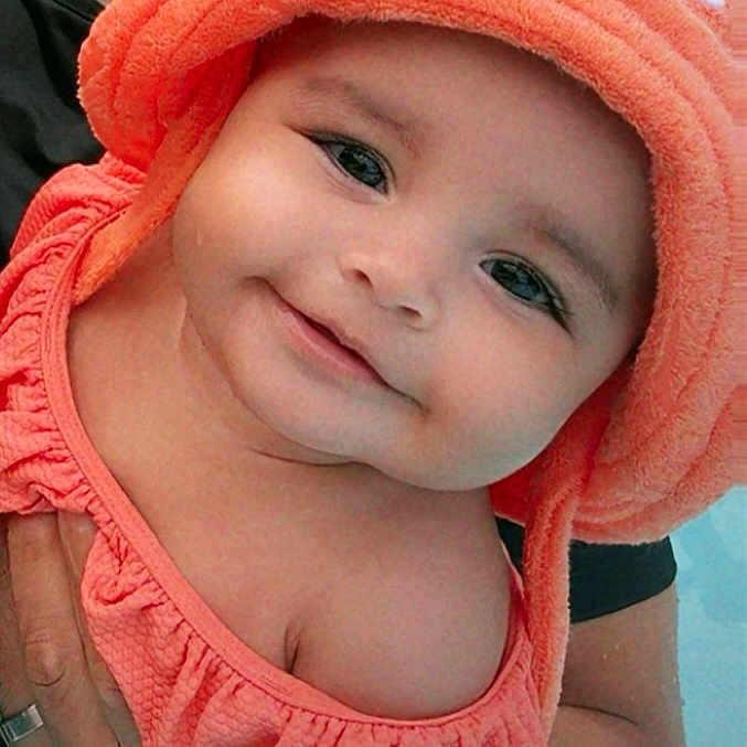 Miyla joined the competition — help win amazing prizes! adult_hand, baby, baby_clothes, child, closeup, cute, face, happy, headwear, holding, infant, orange_clothing, orange_hat, outdoor, person, portrait, skin, smiling, tattoo, water
