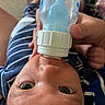 baby, bottle, feeding, hand, blue_clothing, striped_clothing, face, eyes, infant, skin, person, child, mouth, nourishment, closeup, indoors, relaxation, comfort, care, young