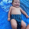 baby, smiling, blue_towel, grass, outdoor, diaper, cloth_diaper, happy, infant, skin, bare_chest, lying_down, small_person, cute, child, summer, nature, relaxed, sunlight, playful