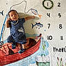 baby, infant, child, milestone_blanket, fishing_theme, fish, boat, numbers, months, wreath, striped_clothing, shark_print, knitted_socks, cute, lying_down, colorful, painted_background, calm, indoors, portrait