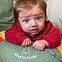 baby, child, face, hair, red_sweater, cushion, polka_dots, blue_eyes, indoor, curious, expression, hands, clothing, person, infant, cute, home, soft_toys, background, portrait