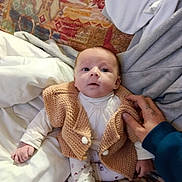 Aïnhoa participe au concours pour gagner de l'argent avec cette photo : baby, infant, newborn, knit_vest, onesie, leggings, blanket, bed, sheet, couch, patterned_background, hand, face, eyes_open, portrait, cozy, indoor, person, sitting, textile