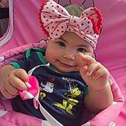 Marleigh is registered to the contest to win money with this photo: baby, child, pink, headband, bow, toy, smile, cute, infant, polka_dot, clothing, seat, playful, face, hand, portrait, indoors, person, happy, closeup