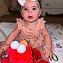 baby, child, bow, headband, dress, plush_toy, elmo, red, toy, indoor, blanket, sitting, person, cute, face, blue_eyes, hand, foot, furniture, home