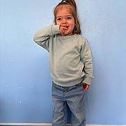 Julia participe au concours pour gagner de l'argent avec cette photo : child, toddler, standing, blue_wall, light_sweater, jeans, rolled_up_jeans, indoor, smiling, playful, casual_clothing, young_child, long_hair, ponytail, happy, cute, person, floor, blue_floor, portrait