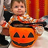 baby, child, infant, portrait, smiling, sitting, pumpkin, halloween, costume, floral_outfit, orange, black, face, eyes, hands, indoor, store, adult, high_chair, seasonal