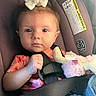 baby, infant, child, car_seat, portrait, bow, white_bow, plush_toy, stuffed_animal, seatbelt, harness, vehicle, car, sitting, looking_at_camera, face, eyes, serious_expression, indoor, close_up