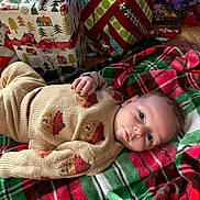 Buck is registered to the contest to win money with this photo: baby, child, infant, blanket, plaid, christmas, presents, gift_wrap, sweater, bear_pattern, floor, wood_floor, holiday, festive, indoors, portrait, cute, looking_at_camera, cozy, warm_clothing