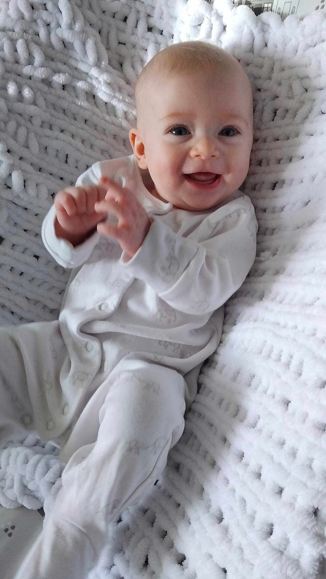 Rita joined the competition — help win amazing prizes! baby, smiling, infant, white_pajamas, blanket, knit_blanket, happy, sitting, face, hands, cute, child, indoor, cozy, portrait, soft_texture, young_child, one_person, light, closeup