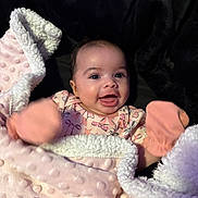 Alaia is registered to the contest to win money with this photo: baby, blanket, pink, mittens, smile, happy, infant, face, cozy, soft, cute, child, portrait, apparel, warm, expression, lying_down, newborn, comfort, indoors