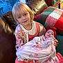 child, baby, couch, blanket, red_bow, plaid_pillow, indoor, cozy, smiling, girl, infant, clothing, portrait, family, holding, cute, warm, happy, home, seated