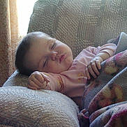 Samantha is registered to the contest to win money with this photo: armchair, baby, blanket, child, comfort, cozy, curtains, cute, furniture, home, indoors, nap, peaceful, person, pink_clothing, relaxing, rest, sleeping, soft_light, toddler