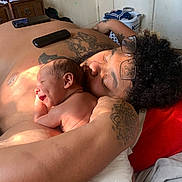 Willow joined the competition — help win amazing prizes! baby, adult, tattoo, smiling, glasses, bedroom, diaper, skin, person, face, arm, hand, furniture, laundry_basket, clothing, hair, light, window_light, indoor, relaxation
