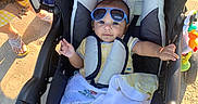 Willow is registered to the contest to win money with this photo: baby, stroller, sunglasses, child, outdoor, sunlight, blanket, toy, person, footwear, sand, hand, clothing, seat, head, smiling, tattoo, accessory, sunshine, relaxation