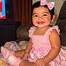baby, child, smiling, pink_bow, pink_dress, socks, blanket, indoor, happy, cute, portrait, sitting, face, infant, home, furniture, colorful, decor, person, toddler
