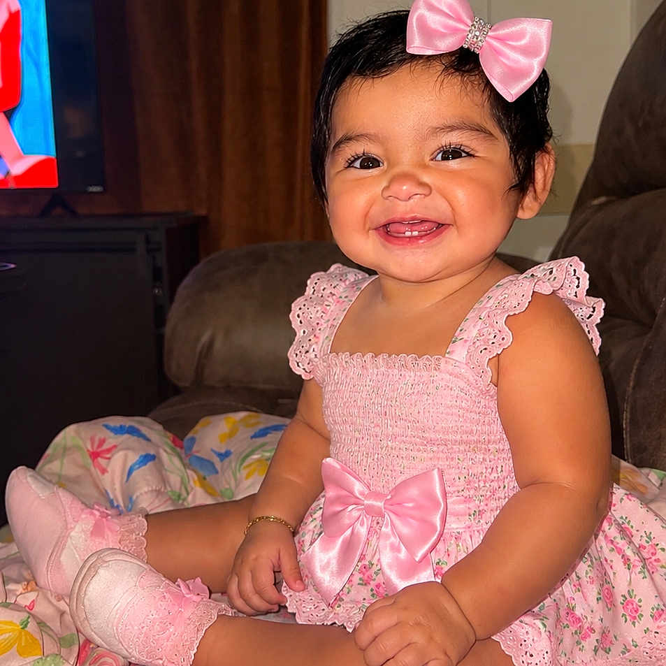Elena joined the competition — help win amazing prizes! baby, child, smiling, pink_bow, pink_dress, socks, blanket, indoor, happy, cute, portrait, sitting, face, infant, home, furniture, colorful, decor, person, toddler