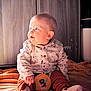 baby, child, infant, sitting, blue_eyes, orange_blanket, patterned_shirt, rust_pants, milestone_card, indoor, wooden_background, cute, hands, socks, portrait, soft_lighting, curious, cozy, young_child, casual_clothing